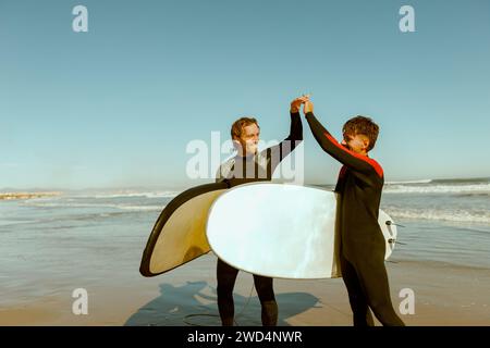 Zwei Surfer begrüßen sich, indem sie sich die Hände schütteln, bevor sie auf den Wellen im Meer surfen Stockfoto