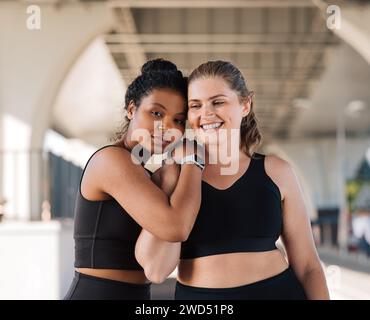 Zwei weibliche Freunde in Übergröße in Sportbekleidung stehen draußen zusammen. Junge Frauen entspannen sich nach intensivem Workout und umarmen sich gegenseitig. Stockfoto