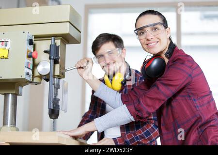 Glücklicher Ingenieur, der weibliche Lehrling in der Verwendung des Bohrers unterweist Stockfoto