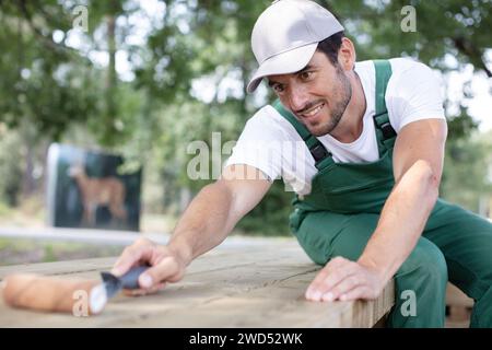 Mann lackiert Naturholzbank mit einem Pinsel im Park Stockfoto