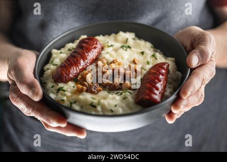 Die Hände eines älteren Hauskochs halten einen Teller mit einem nationalen slowakischen Gericht - Bryndzove Halusky. Stockfoto