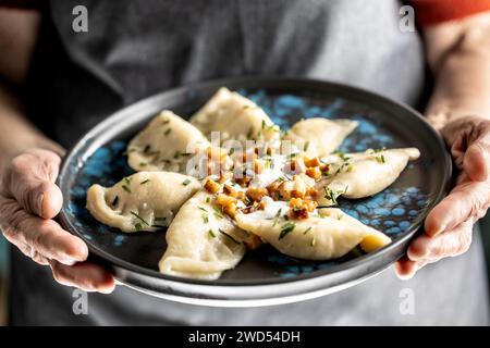 Die Hände eines älteren Hauskochs halten einen Teller mit einem nationalen slowakischen Gericht - Bryndzove Pirohy. Stockfoto