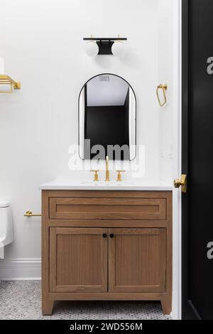 Ein Badezimmer mit Holzschrank, goldenem Wasserhahn und Akzenten, schwarzer Tür und rundem Marmorboden. Stockfoto