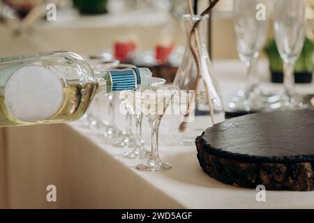 Kellner gießt Martini oder Champagner in Kristallgläser auf der Tischparty bei der Hochzeitsfeier Stockfoto
