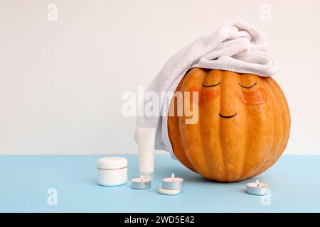 Kürbis mit gezeichnetem Gesicht, Spa-Zubehör und Flecken unter den Augen auf blauem Tisch Stockfoto