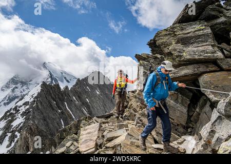 Zwei Bergsteiger auf einem mit einem Seil gesicherten Wanderweg, vergletschter Gipfel großer Moeseler im Hintergrund, Abfahrt vom Gipfel Schönbichler Stockfoto