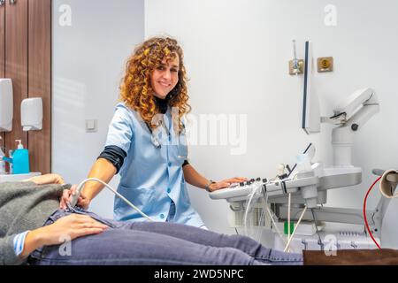 Ärztin lächelt in die Kamera, während sie einen Ultraschall zu einer schwangeren Frau in das Krankenhaus durchführt Stockfoto