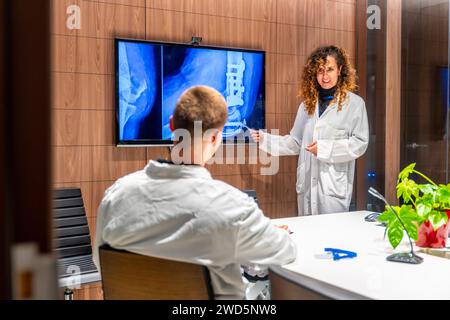 Zwei junge kaukasische Ärzte tragen weiße Labormäntel, untersuchen ein Röntgenbild und sprechen im Krankenhaus Stockfoto