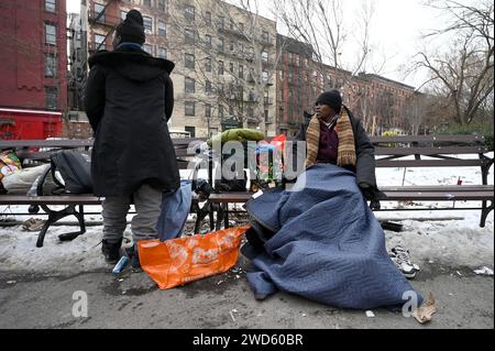 Ein Asylsuchender aus Westafrika spricht mit einem anderen Migranten (zurück zur Kamera), während er auf einer Bank im Tompkins Square Park sitzt, die mit einer gespendeten Schiffsdecke gegenüber von St. Brigid Pensionierungszentrum auf der Lower East Side in Manhattan, New York, NY, 18. Januar 2024. Meist warten allein stehende Männer auf einen neuen Unterschlupf, nachdem vor kurzem eine Begrenzung von 30 Tagen auferlegt wurde, was sie zwingt, sich erneut zu bewerben und zu warten; Schätzungen zufolge kommen etwa 3000 Migranten pro Woche in New York City an. (Foto: Anthony Behar/SIPA USA) Stockfoto