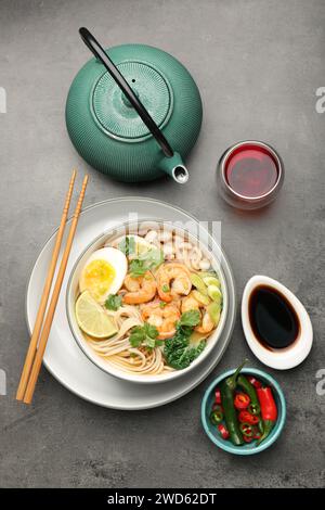 Köstliche Ramen mit Garnelen und Ei in Schüssel serviert auf grauem Tisch, flach gelegt. Nudelsuppe Stockfoto