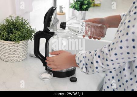Frau, die Essig aus der Flasche in den elektrischen Wasserkocher in der Küche gießt, Nahaufnahme Stockfoto