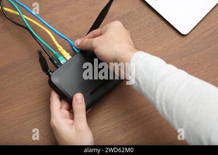 Mann, der Kabel in den WLAN-Router am Holztisch einführt, Nahaufnahme Stockfoto