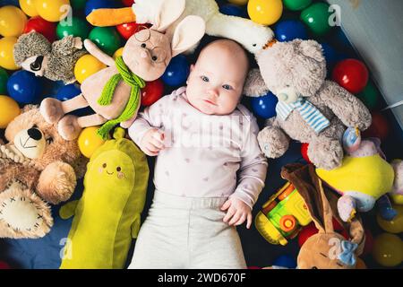 Blick von oben auf das niedliche Baby, das auf dem Boden zwischen bunten Spielzeugen liegt. Stockfoto