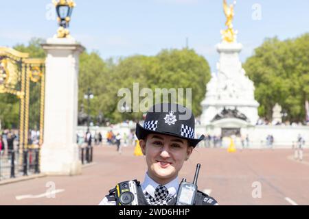 Eine lächelnde Polizistin vor dem Buckingham Palace, London. Hinter ihr steht das Victoria Memorial. Stockfoto