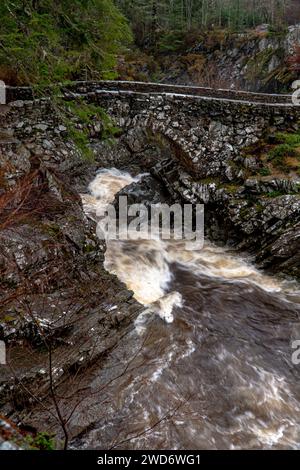 Eine malerische Brücke, die sich anmutig über einen ruhigen Fluss inmitten eines üppigen Waldes in Schottland spannt Stockfoto