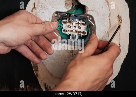 Austauschen und Installieren einer neuen Steckdose. Hände mit einem Schraubenzieher männlicher Elektriker auf dem Hintergrund der Wand im Haus, die Reparaturen macht Stockfoto