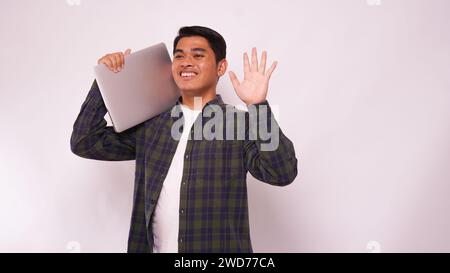 Asiatischer Student hebt den Laptop auf seiner Schulter auf weißem Hintergrund Stockfoto