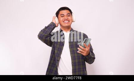 Asiatischer junger Mann, der Musik auf dem Smartphone mit schnurlosen Kopfhörern vor weißem Hintergrund hört Stockfoto