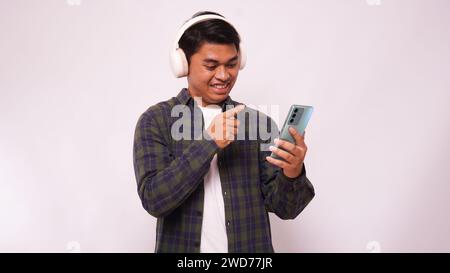 Asiatischer junger Mann, der Musik auf dem Smartphone mit schnurlosen Kopfhörern vor weißem Hintergrund hört Stockfoto