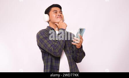Asiatischer junger Mann, der Musik auf dem Smartphone mit schnurlosen Kopfhörern vor weißem Hintergrund hört Stockfoto