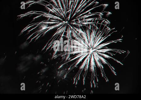 Feuerwerk am Nachthimmel. Explosionen der Pyrotechnik beim Festival. Schwarzweißfoto mit 3D-Glitcheffekt Stockfoto