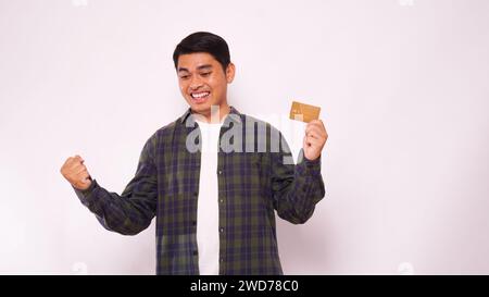Junger asiatischer Mann, der glücklich lächelt, wenn er nach einer Kreditkarte sucht, die er hält Stockfoto