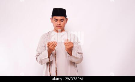 Asiatischer muslimischer Mann, der Gebetsperlen hält und vor weißem Hintergrund betet Stockfoto