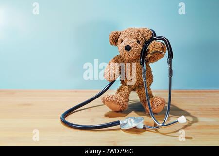 Stehender Teddybär, der ein Stethoskop auf einem Holztisch vor türkisfarbenem Hintergrund hält, Kinderkonzept für Gesundheitsfürsorge, Arzt und Kinderarzt Stockfoto