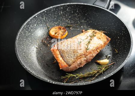 Regenforellenfilet mit knuspriger frittierter Haut, Knoblauch, Zitrone und Kräutern in einer Pfanne, gesundes Kochen mit Fisch, Kopierraum, ausgewählter Fokus, schmale Dep Stockfoto