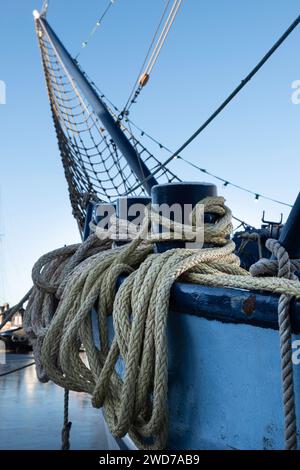 Die Seile des Schiffes sind um die eisernen Schiffspoller auf dem Geländer eines Segelbootes aus Metall mit einem Jib-Netz am Bug verdreht. Konzentrieren Sie sich auf die Seile Stockfoto