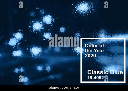 Hauptfarbe Trend 2020 klassisches Blau. Nachtstadt mit verschwommenem Licht von Autos und Taschenlampen durch das Glas mit Regentropfen Stockfoto