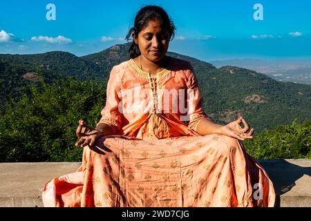 Eine Inderin in einem lebendigen Sari sucht Trost und spirituelle Verbindung durch Meditation inmitten der beeindruckenden Aussicht auf den Berg Stockfoto