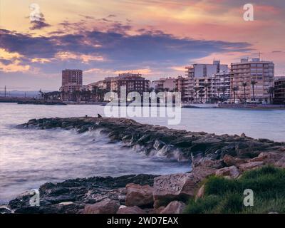 Torrevieja, Alicante, Spanien. Hinter einem einsamen Fischer auf der Mole flimmern die Lichter der Stadt Torrevieja an, während die Sonne über dem Mittelmeer untergeht Stockfoto