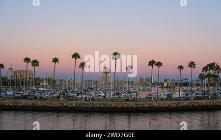 Ein atemberaubender Blick auf den Sonnenuntergang auf einen Hafen mit Palmen, die sich gegen den Himmel schmiegen und sich im Wasser spiegeln Stockfoto