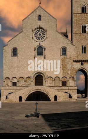 Die Westfront der romanisch-apulischen Kathedrale begann 1099, die Cattedrale di San Nicola Pellegrino oder Basilica Cattedrale di Santa Maria Assunta, in Trani an der Adriaküste in Apulien (Apulien), Italien. Eine Treppe führt zu einem reich gestalteten Portal mit Bronzetüren aus den späten 1100er Jahren. Zu beiden Seiten der Türen durchziehen blinde Arkaden mit zylindrischen Schäften und fein geschnitzten Kapitellen die Fassade. Das obere Stockwerk ist von einem Rosenfenster und mehreren kleineren Rundbogenfenstern durchbrochen, alle mit geschnitzten Umrandungen. Stockfoto