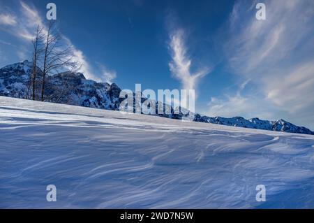 Starker Wind erzeugt Wellen auf dem Schnee, mit schneebedeckten Bergen im Hintergrund. Stockfoto