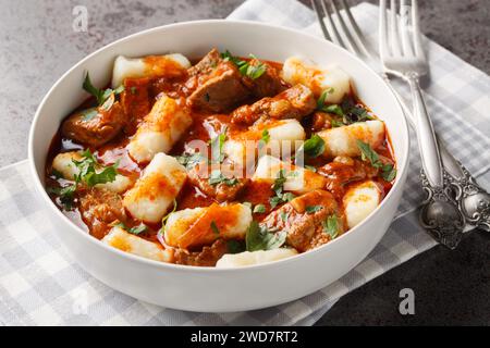 Hausgemachte traditionelle polnische Kartoffelknödel kopytka serviert mit Fleischeintopf in Nahaufnahme auf einem Teller auf dem Tisch. Horizontal Stockfoto