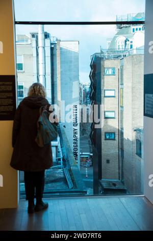 Blick von der Fotografen Galerie Ausstellung. Fotos im Zimmer auf der höheren Etage und der Schriftzug „Soho Photography Quarter“ auf dem Gebäude. London. UK. (137) Stockfoto