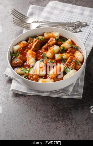 Polnische traditionelle Kartoffelknödel Kopytka mit Gulasch in Nahaufnahme auf einem Teller auf dem Tisch. Vertikal Stockfoto