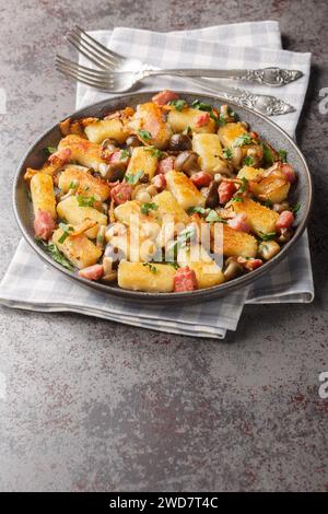 Polnische gebratene Kartoffelknödel Kopytka mit Speck, Zwiebeln und Pilzen in Nahaufnahme auf einem Teller auf dem Tisch. Vertikal Stockfoto