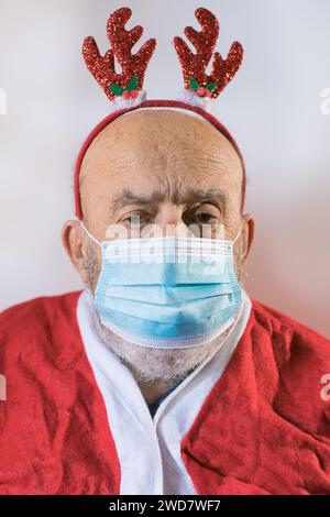 Älterer Mann im Weihnachtsmann-Anzug mit Gesichtsmaske und Rentierohren Stockfoto