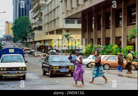 Elfenbeinküste, Abidjan; zwei Frauen mit Körben gefüllt mit Früchten, die eine Straße überqueren. Stockfoto
