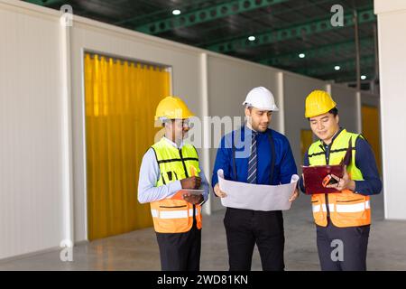 Das Team der Ingenieure, das mit der Arbeit des Architekten arbeitet, inspiziert das Bauprojekt der großen Gebäudefabrik mit Grundriss Stockfoto