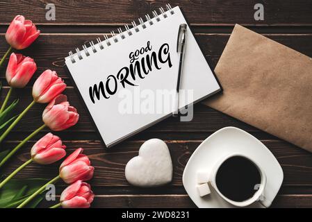 Grußkarte mit der Aufschrift Guten Morgen. Strauß aus rosa Tulpenblüten mit einer Tasse Kaffee auf hölzernem Hintergrund Stockfoto