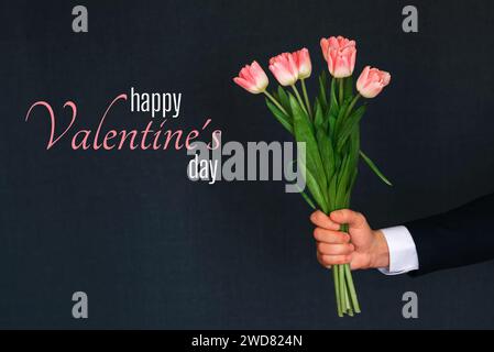 Grußkarte mit der Aufschrift Happy Valentine's Day. Strauß rosa Tulpenblüten in der Hand eines Mannes Stockfoto