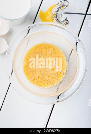 Rührei in einer Glasschale mit einem Glas Milch. Zubereitung von Mischen von Eiern auf einem Holztisch als hausgemachtes Essen. Draufsicht mit flacher Lage. Stockfoto