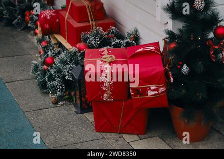 Große rote Geschenkboxen mit Bändern stehen neben einem weißen Holzrahmenladen auf dem Asphalt. Nahaufnahme der Landschaft, Weihnachtsmarkt im Stadtzentrum Stockfoto