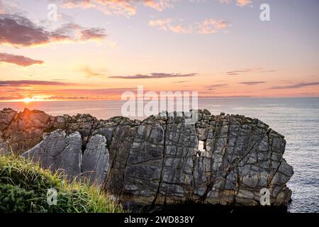 Steile Klippe mit fensterartiger Höhle, die durch Erosion gehauen wurde. Wunderschöne Küstenlandschaft bei Sonnenuntergang an der Broken Coast von Liencres, Kantabrien, Spanien Stockfoto