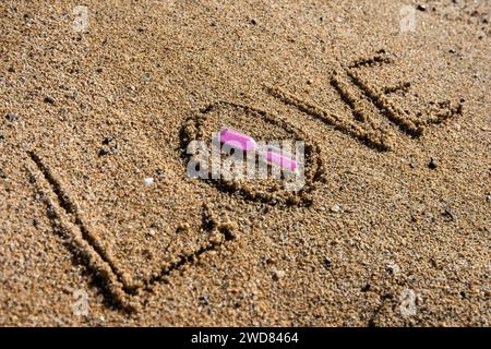 Zeitlose Liebe: „Liebe“ am Strand in einer rosafarbenen Sanduhr, wo Romantik auf den Sand ewiger Momente trifft Stockfoto