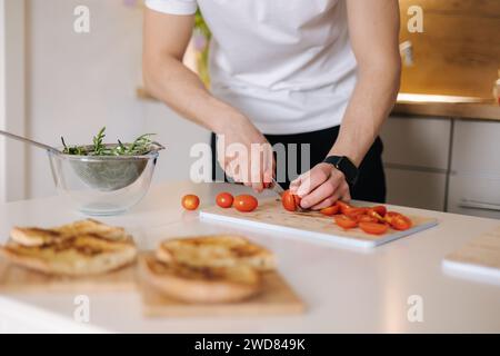 Ein gutaussehender Mann schneidet kleine Bio-Tomaten auf Holzbrett. Rote Kirschtomate Stockfoto